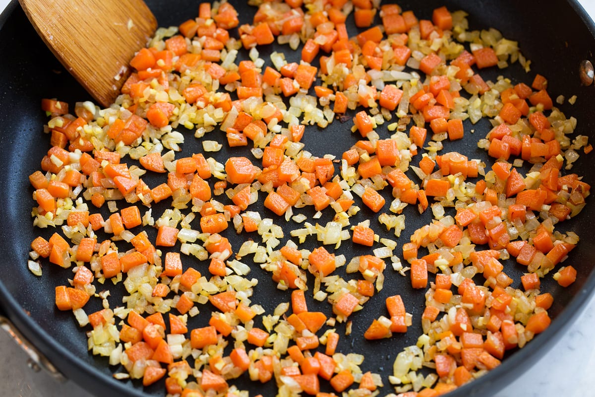 Sautéing carrots, onions, ginger and garlic in a skillet.
