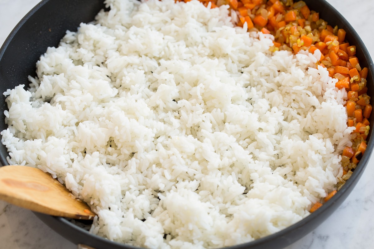 Frying white rice in a skillet with vegetables.