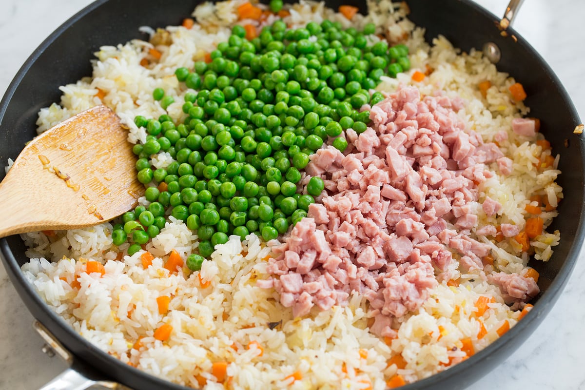 Peas and ham added to fried rice mixture in skillet.