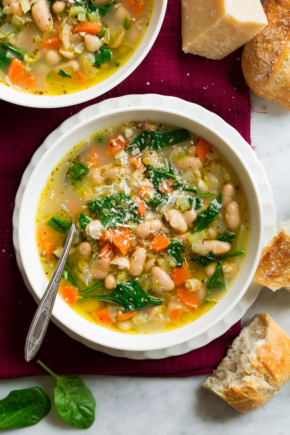 White bowl with tuscan bean soup set over a white scalloped plate and a red napkin.