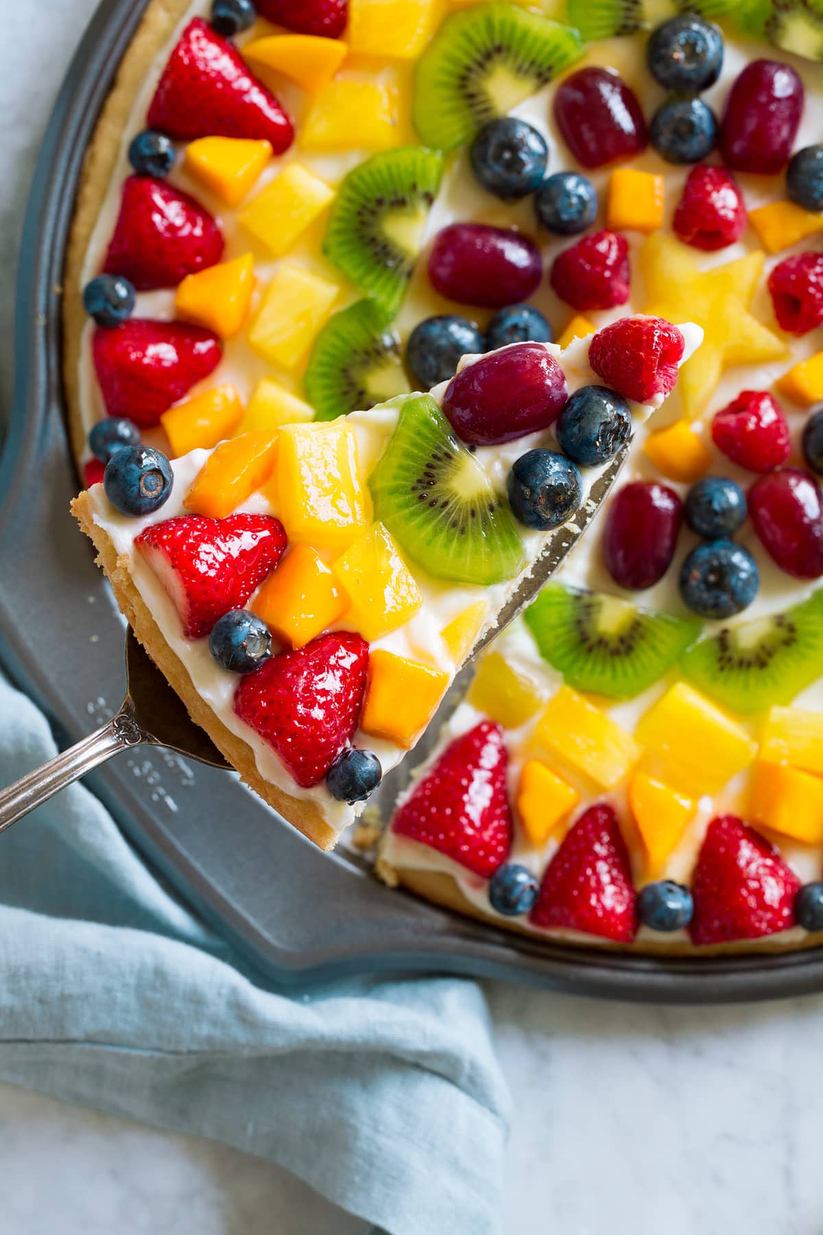 Overhead image of fruit pizza with slice cut and lifted out.