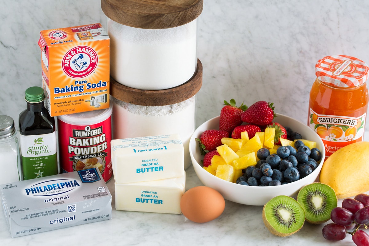 Image of fruit pizza ingredients including flour, sugar, baking powder, baking soda, vanilla, egg, cream cheese, salt, fresh fruit and jam.
