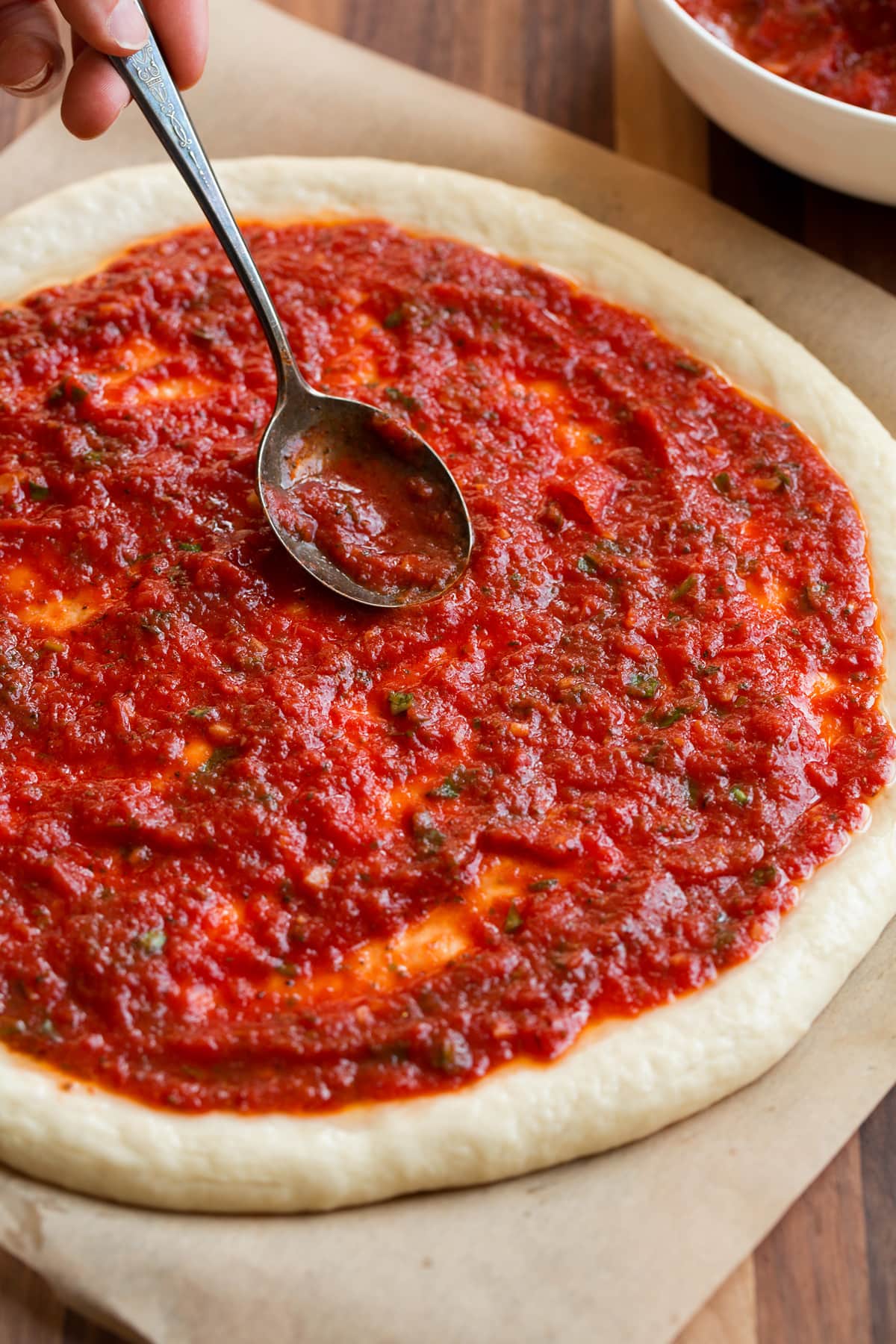 Spooning homemade pizza sauce over a round of pizza dough.