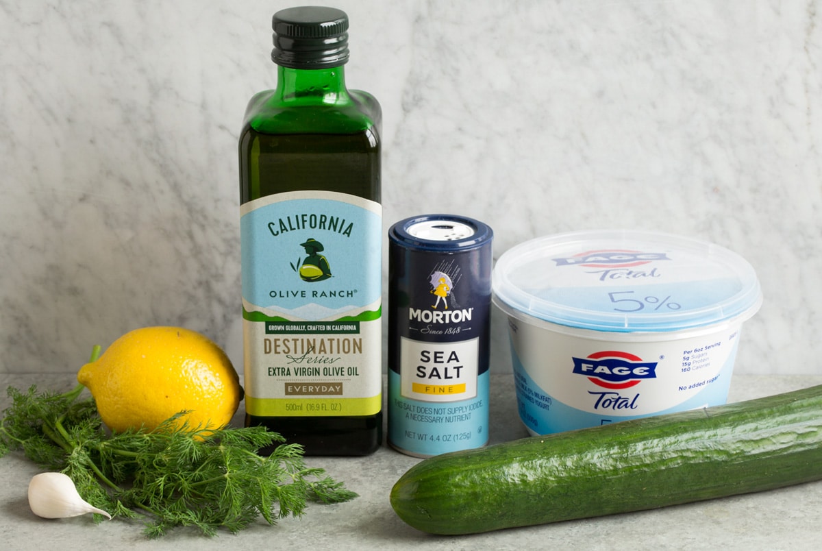 Image of ingredients used to make tzatziki sauces. Includes Greek yogurt, cucumber, salt, lemon, olive oil, dill and garlic.