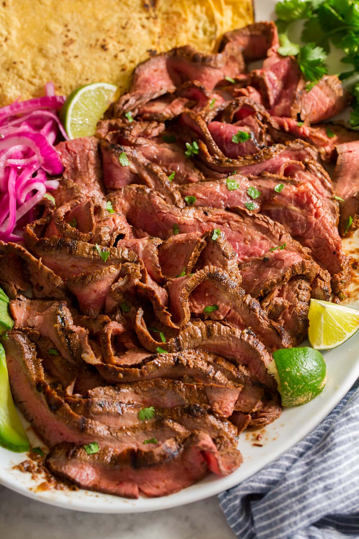 Sliced strips of carne asada shown on a white platter from a side view.