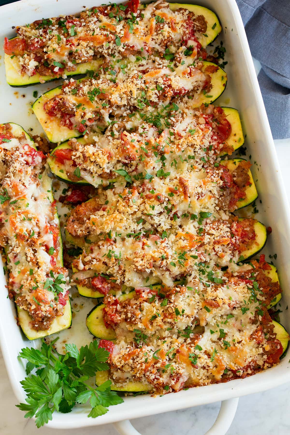 Overhead image of stuffed zucchini boats in a road in a white baking dish.