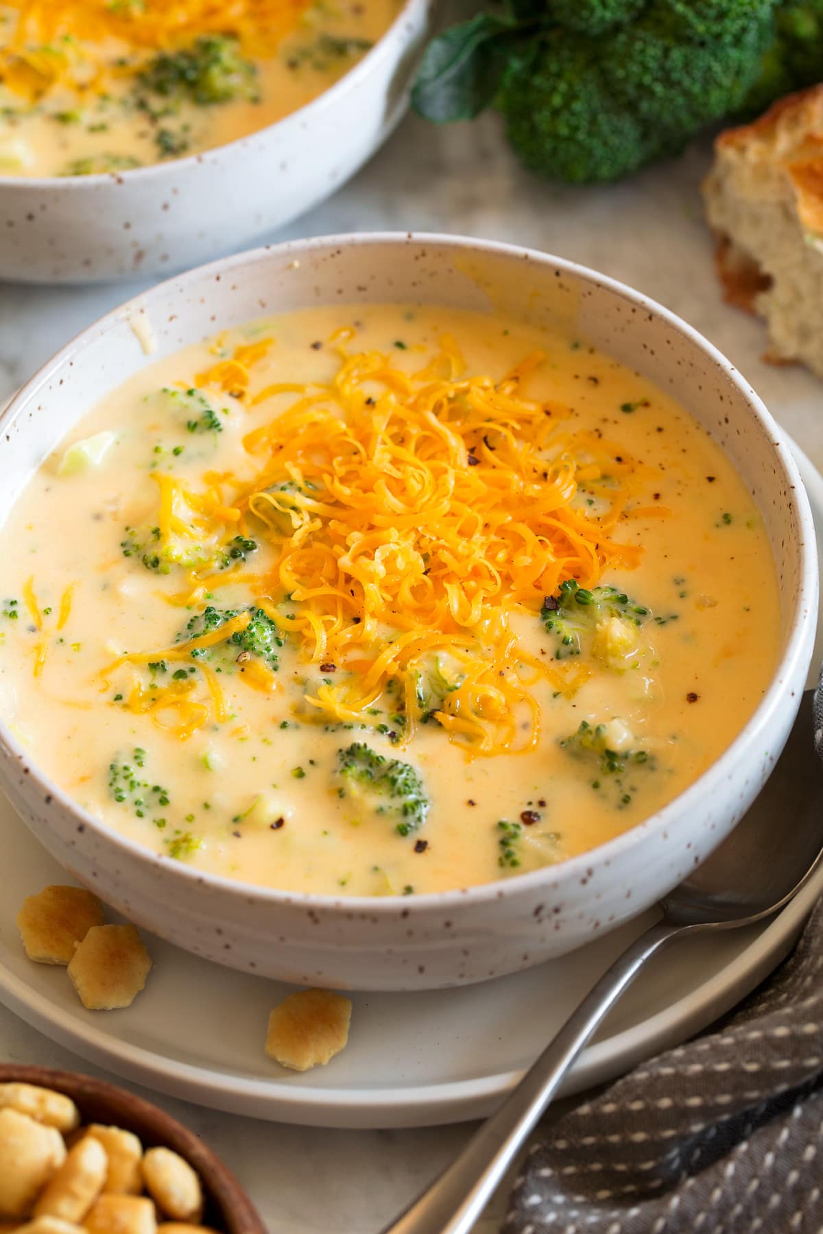 Single serving of broccoli cheese soup in a white bowl with crackers to the side.