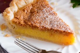 Slice of chess pie on a white dessert plate with fall leaves surrounding plate.