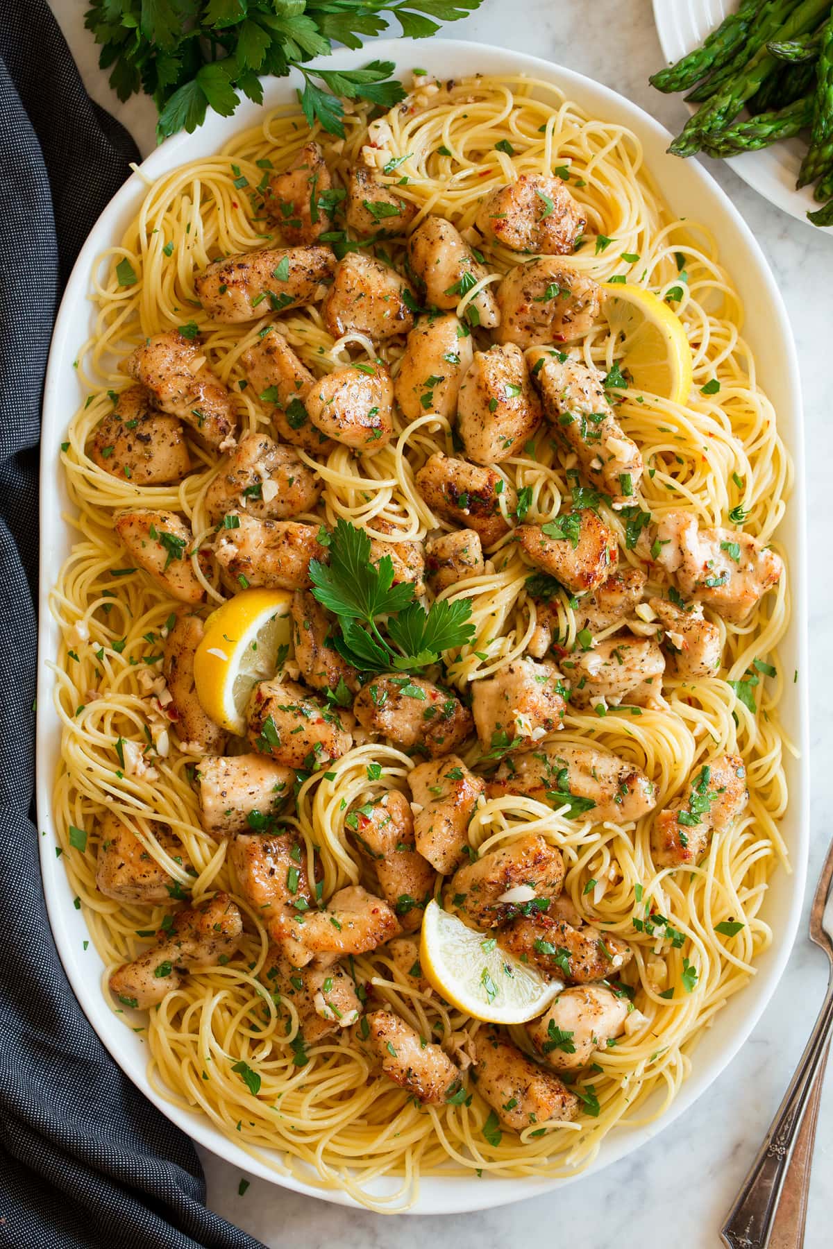 Chicken scampi shown on an oval serving platter. Includes thin spaghetti, lemon, browned chicken pieces and parsley.