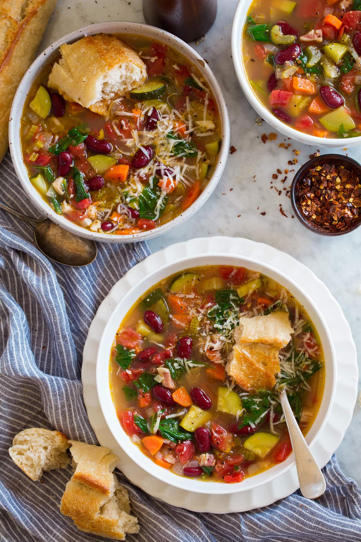 Overhead images of two servings of minestrone soup in white bowls set over a marble surface.