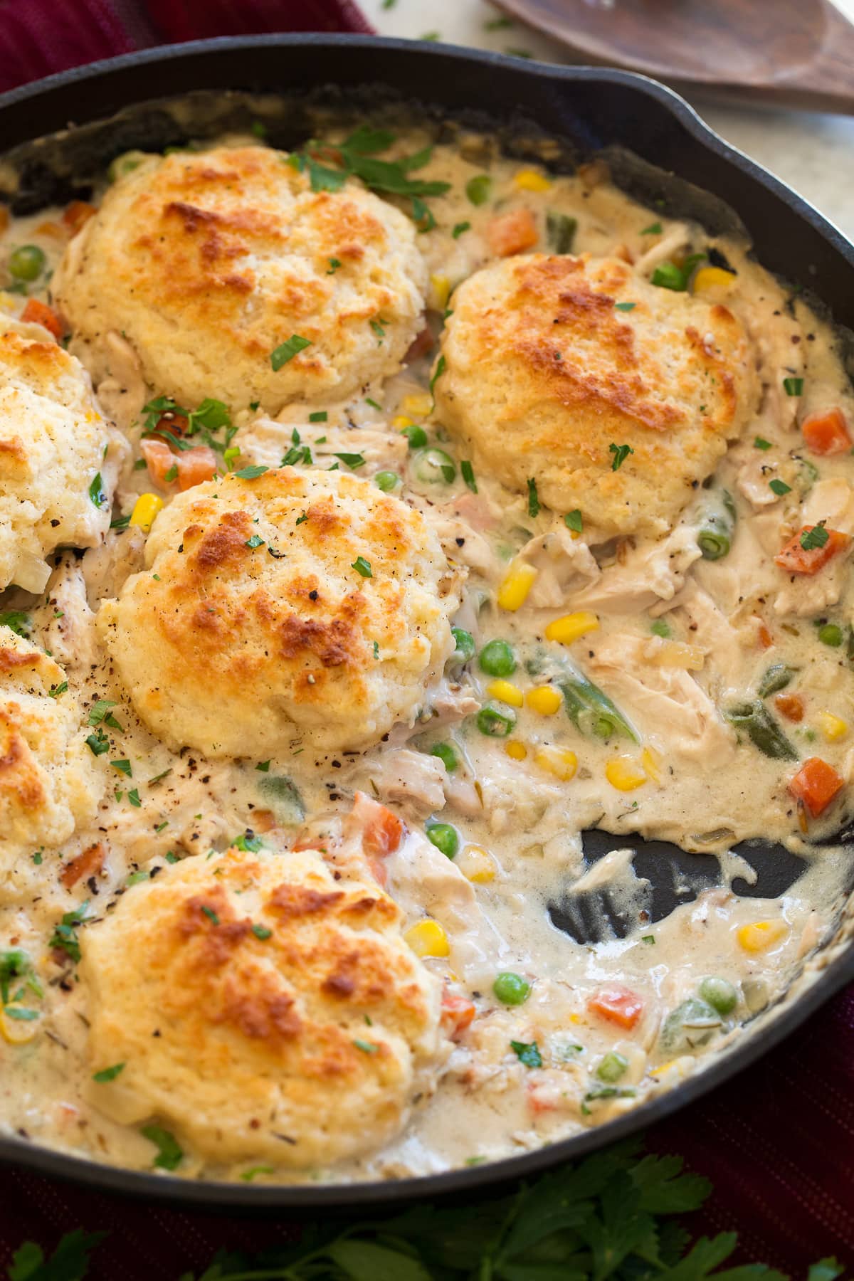 Image of Chicken Pot Pie with Biscuits shown in a cast iron skillet with a scoop removed from pot pie.