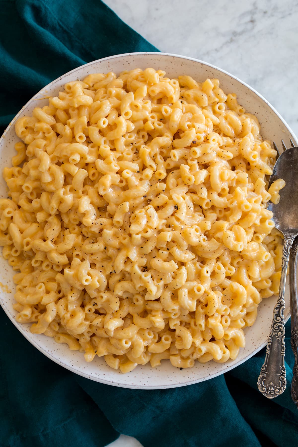 Overhead image of Instant Pot Mac and Cheese in a speckled white ceramic bowl set over a turquoise kitchen cloth.