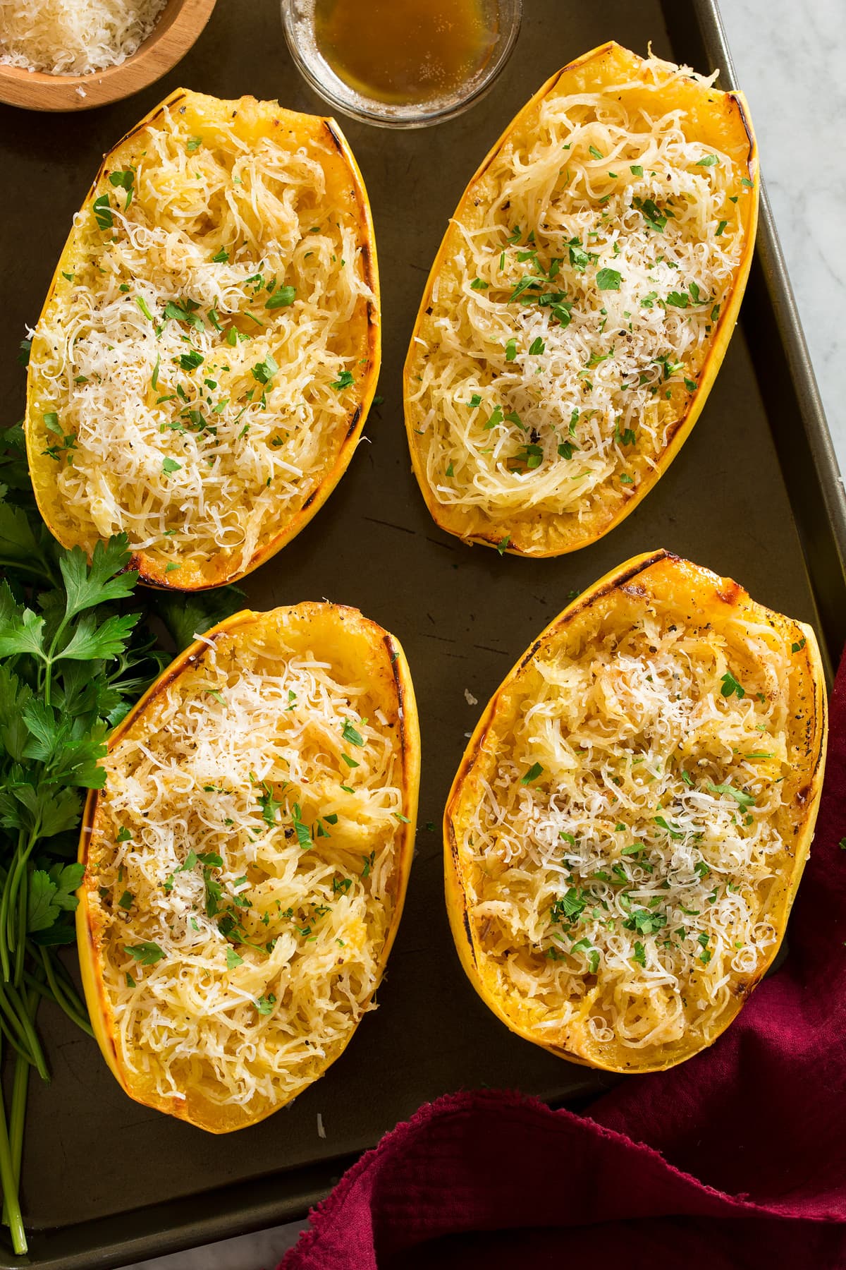 Overhead image of four roasted spaghetti squashes on a dark baking sheet.