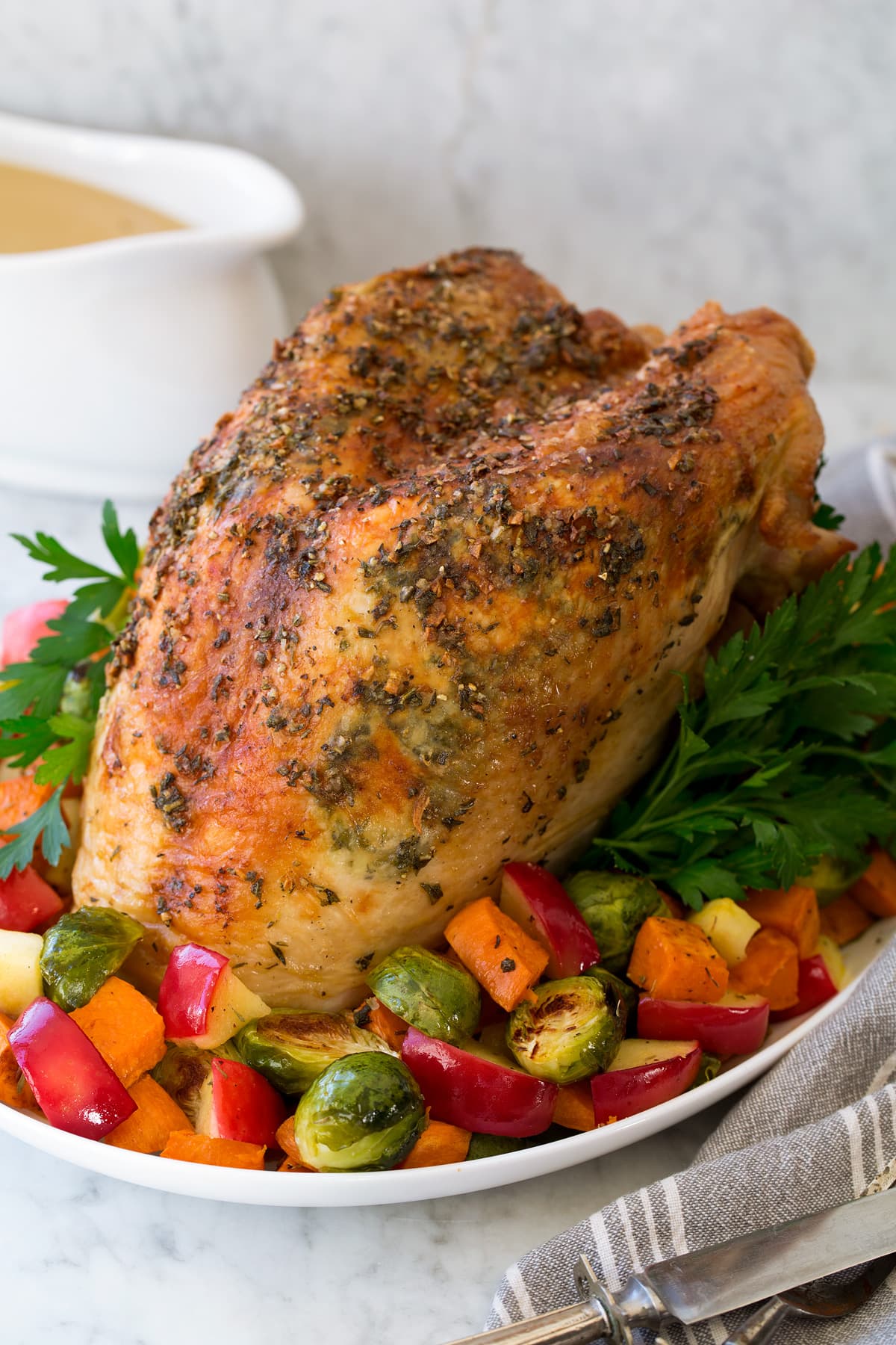 A whole Roast Turkey Breast shown on a platter with roasted vegetables and herbs.