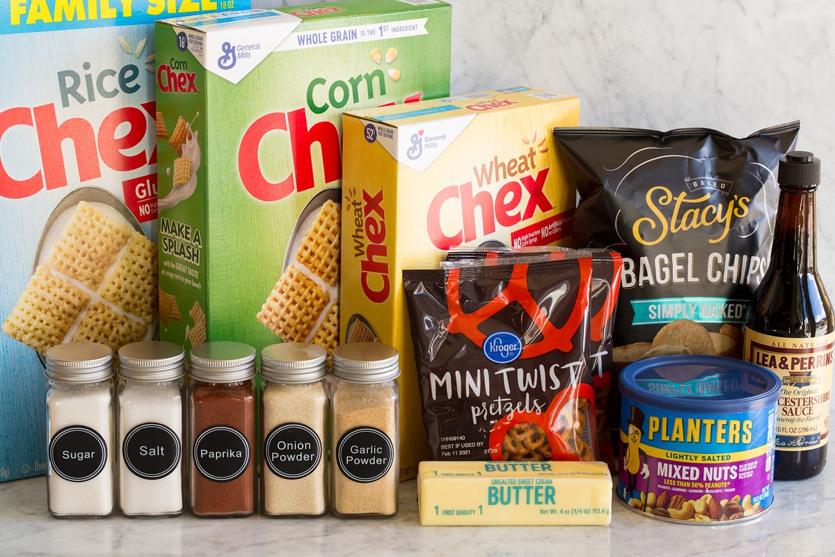 Image of ingredients used to make Chex Mix. Shows rice, corn and wheat Chex cereal, bagel chips, Worcestershire sauce, mixed nuts, pretzels, butter, and spices in jars.