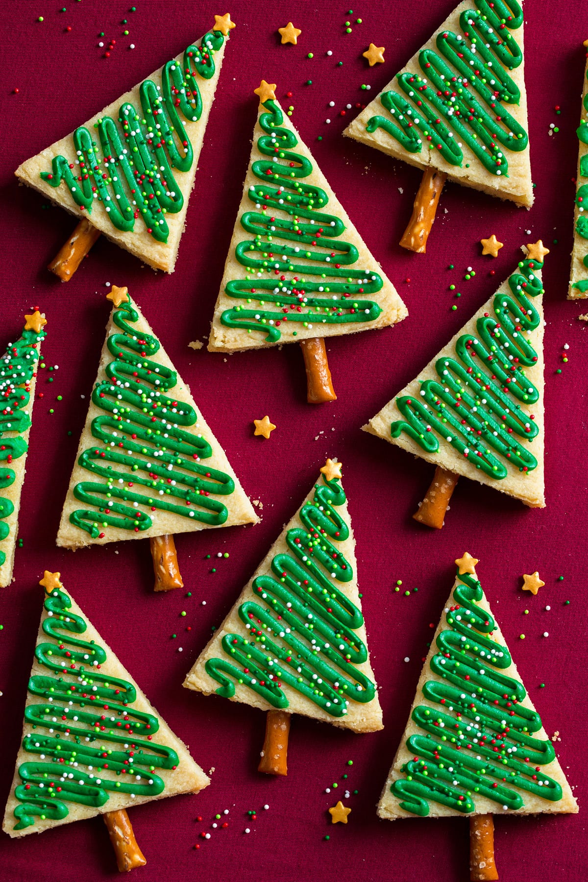 Triangular decorated Christmas tree cookies shown on a red surface.