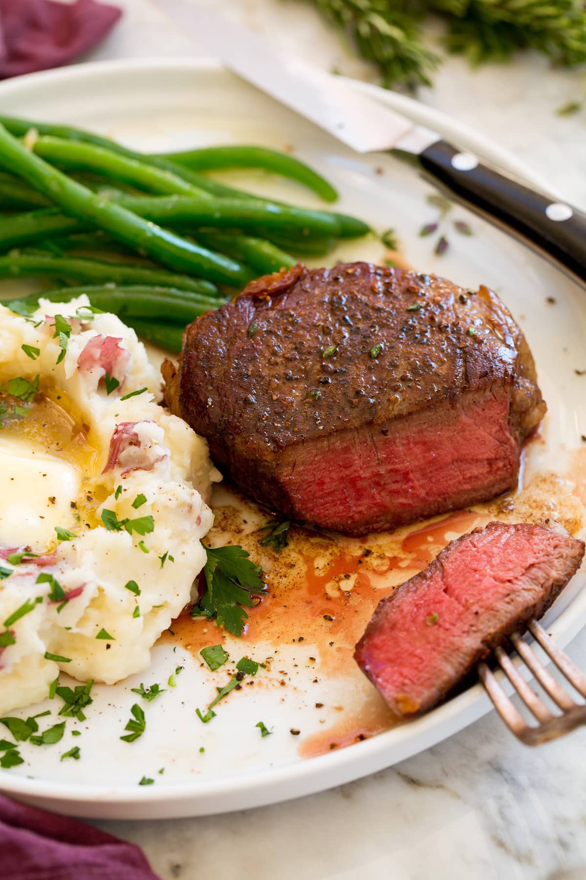 Filet Mignon shown on a serving plate with a side of mashed potatoes and steamed green beans.