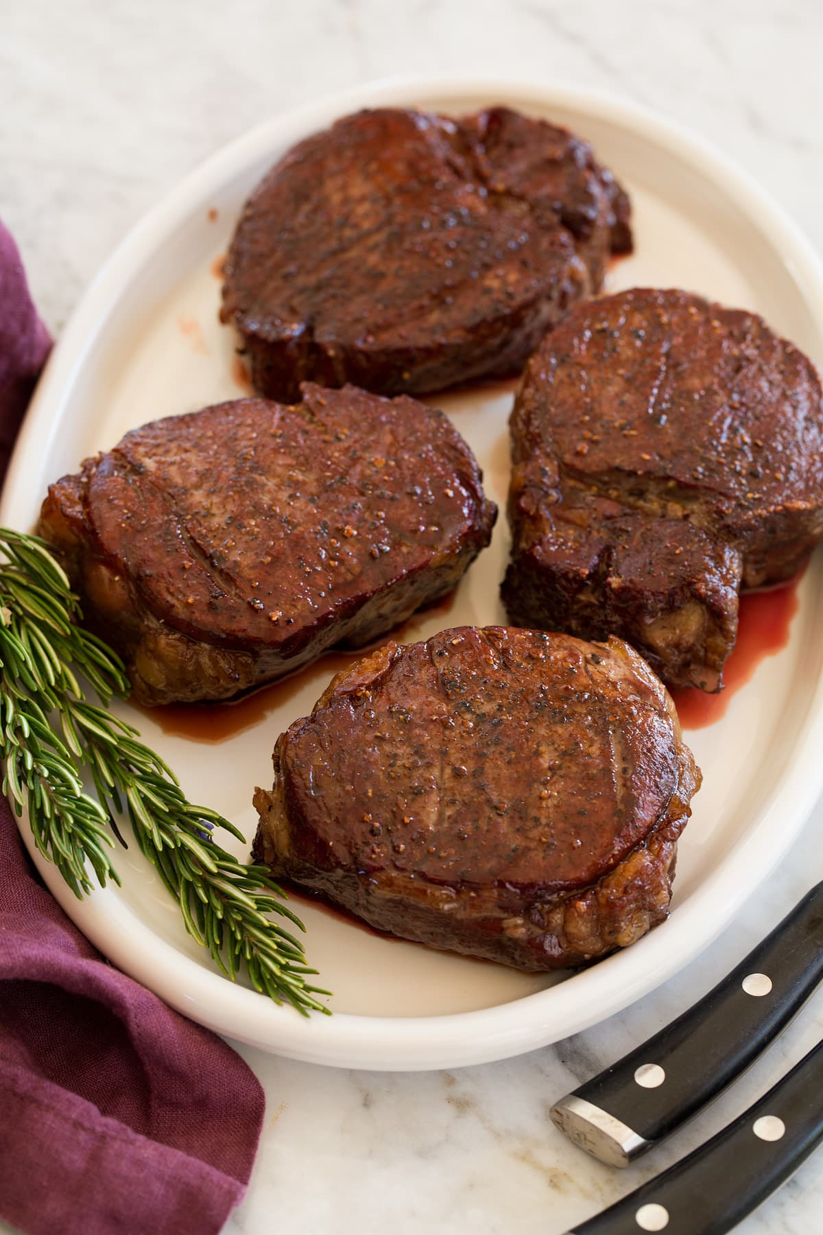Four cooked fillet mignon steaks on a serving platter.