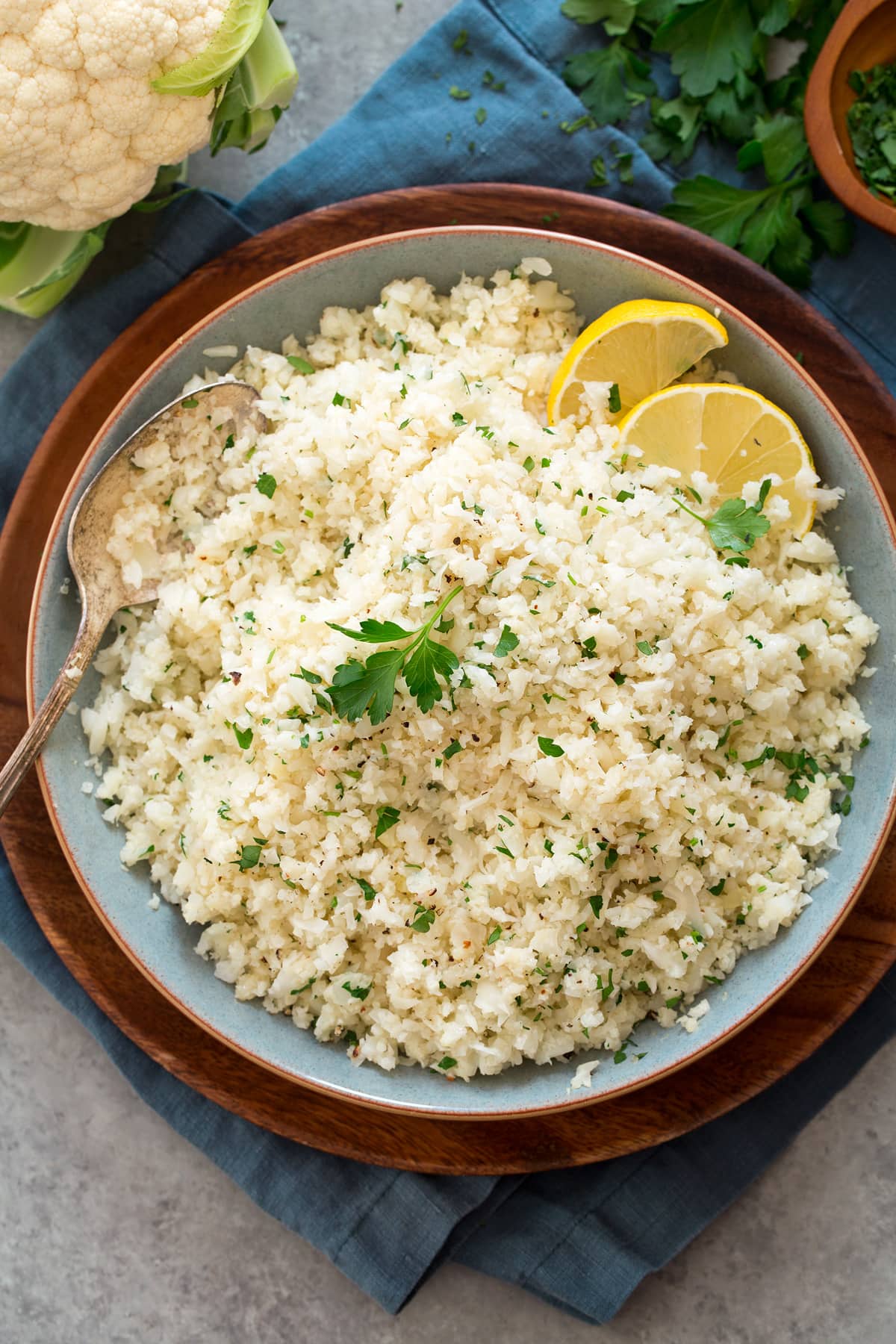 Overhead photo of cauliflower rice in a blue bowl set over a wooden plate.