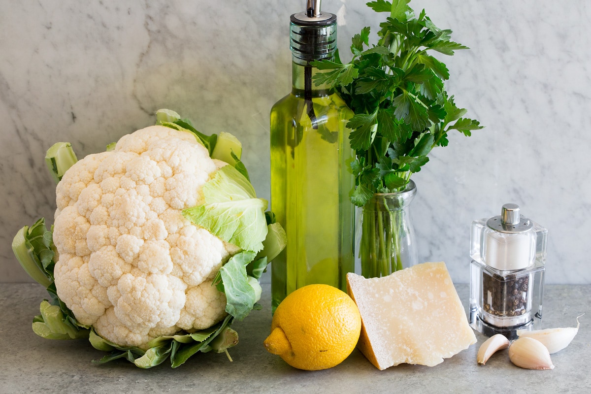 Photo of ingredients used to make cauliflower rice. Includes fresh cauliflower, olive oil, parsley, garlic, parmesan, lemon, salt and pepper.