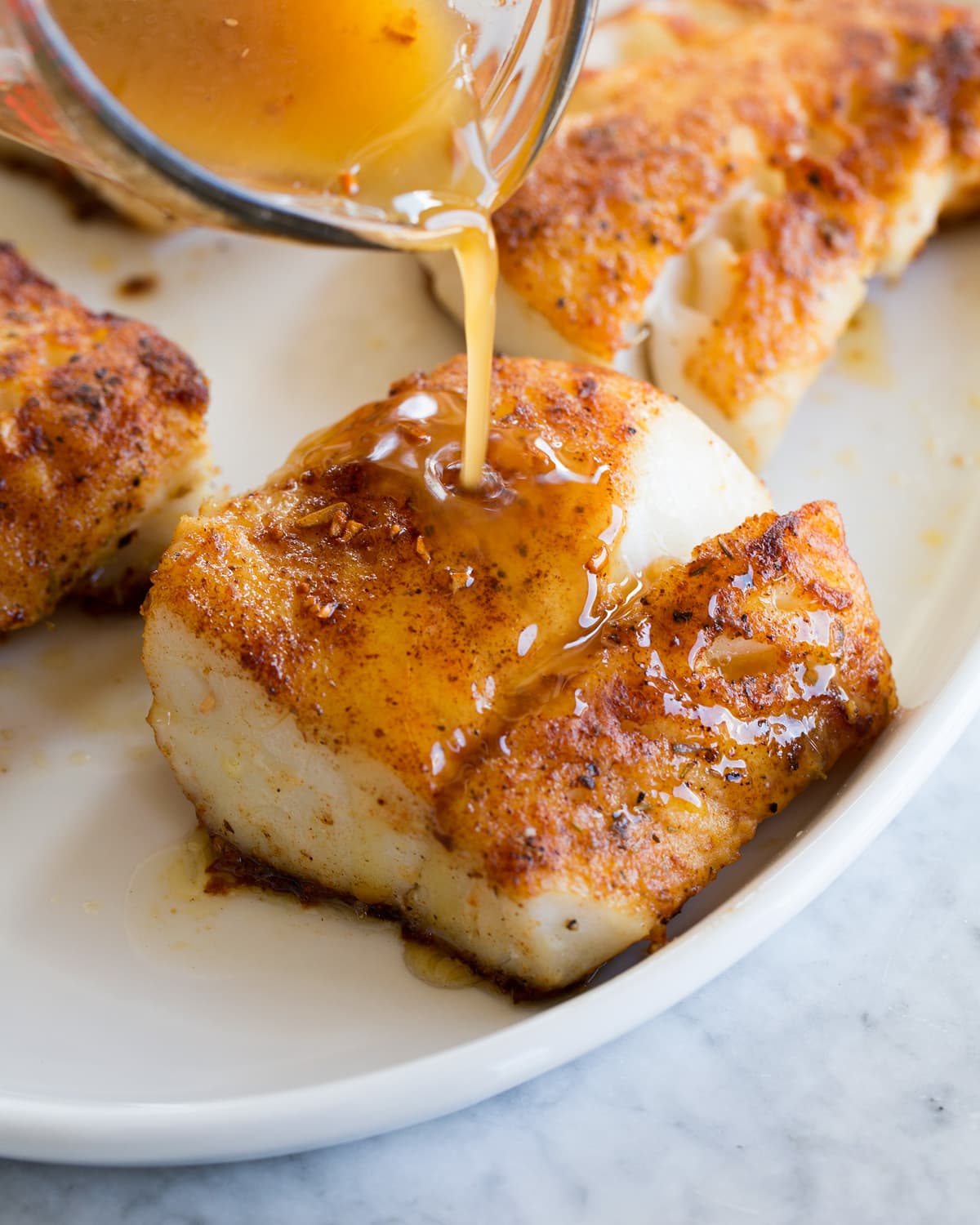 Sauce being poured over cooked white fish fillet on a platter.