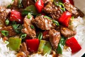 Photo: Pepper Steak in a bowl over white rice. Bowl is resting on a dark green cloth over a marble surface.
