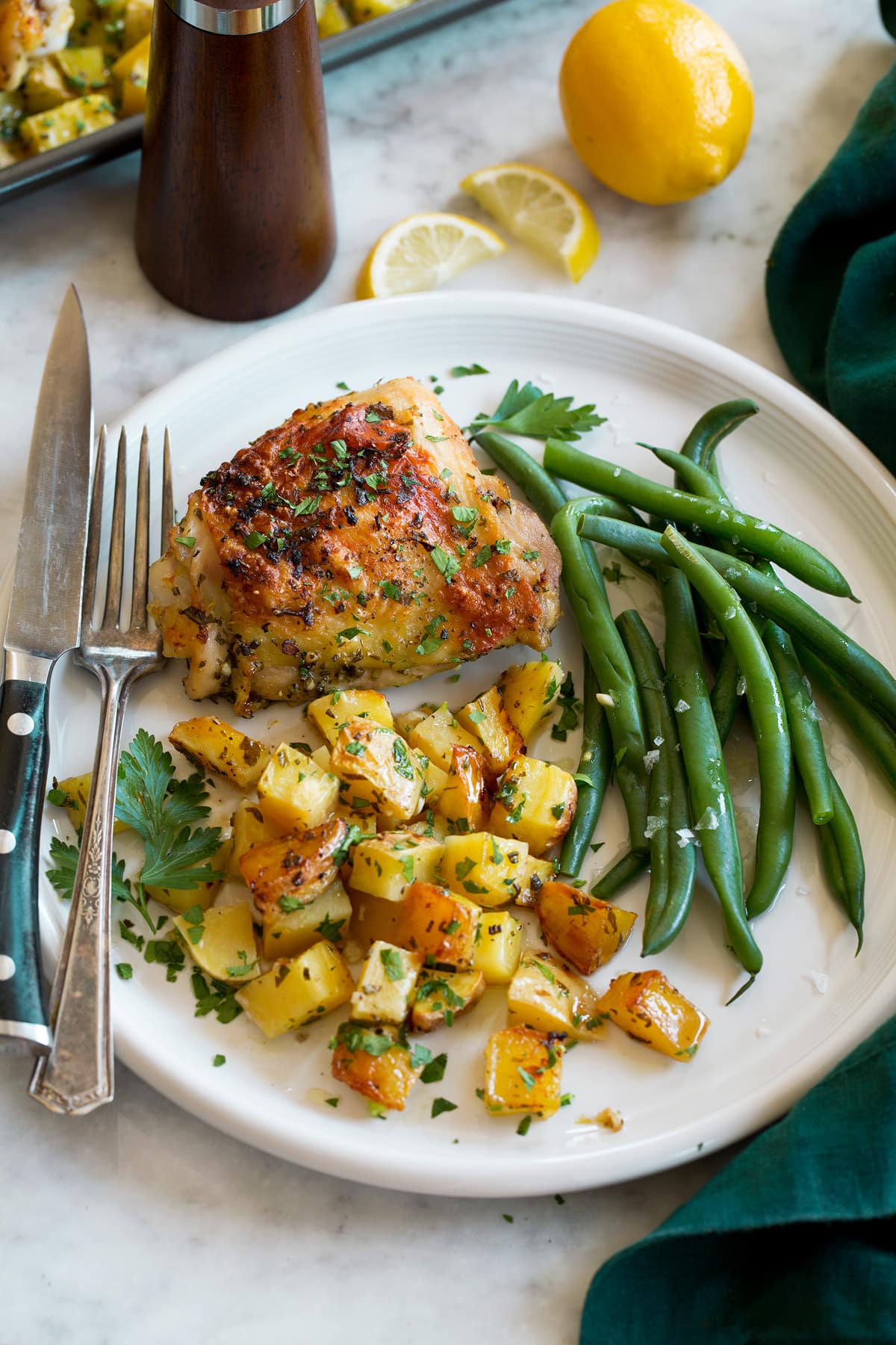 Serving of chicken and potatoes on a white dinner plate shown with a side of steamed green beans as a serving suggestion.