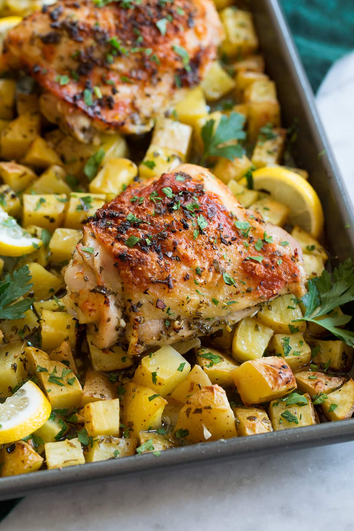 Close up photo of lemon chicken thighs and potatoes on a baking sheet.