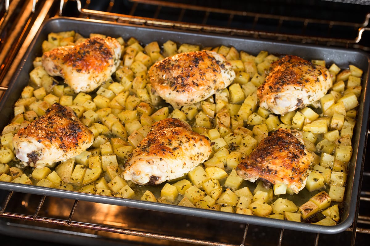 Chicken and potatoes baking in the oven on a baking sheet.