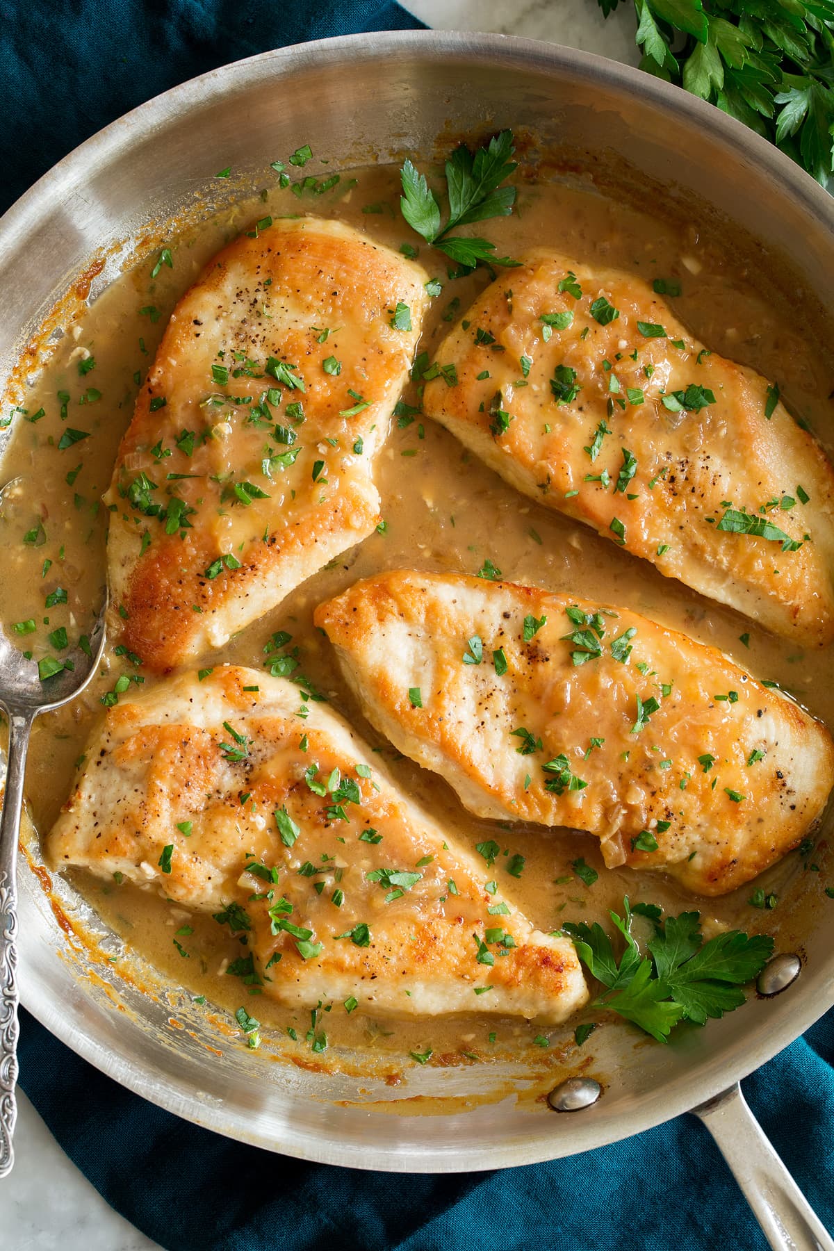 Four portions of chicken in white wine sauce shown in a stainless steel skillet.