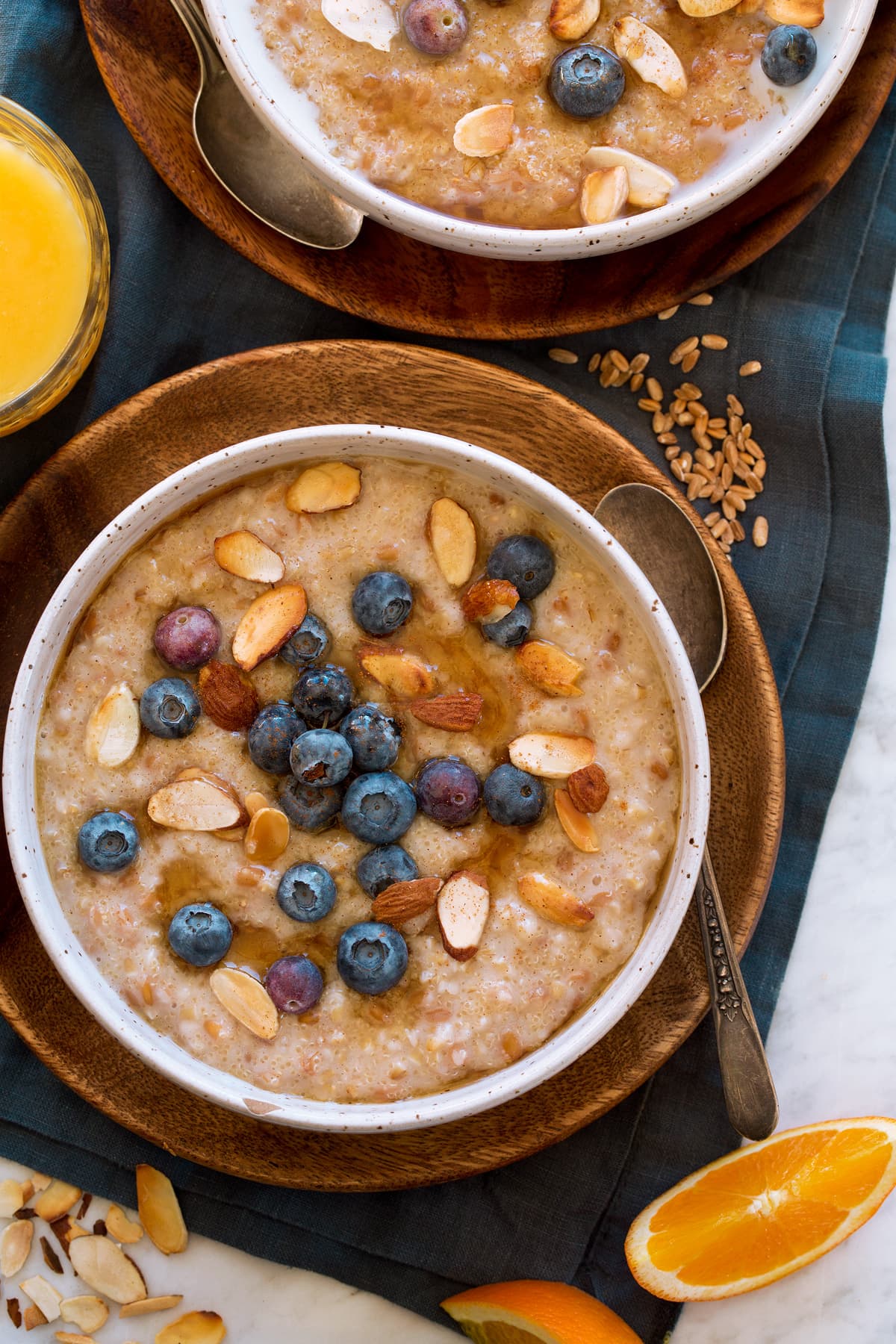 Porridge shown in a white bowl over a wooden plate with dried grains to the side. It is shown served with orange juice.