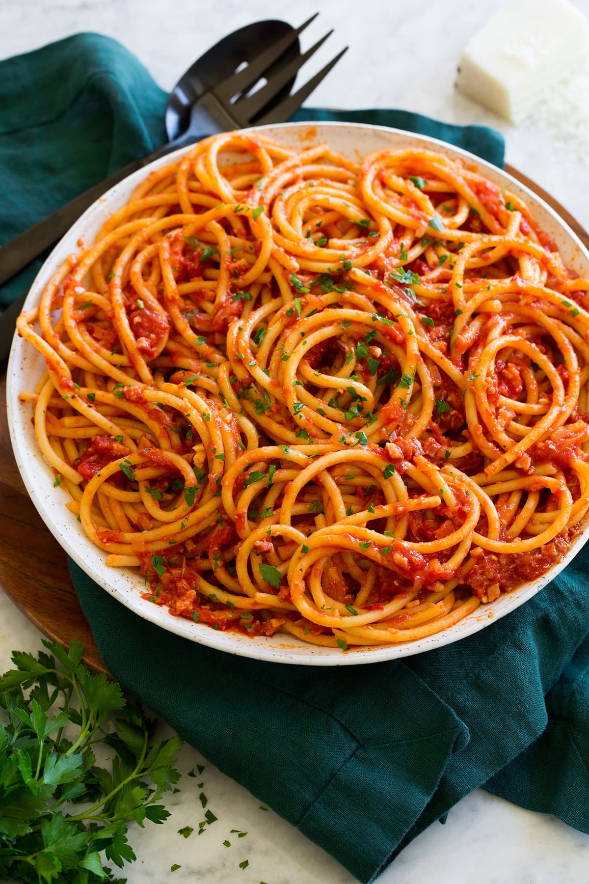 Bucatini with amatriciana sauce in a white serving bowl with parmesan cheese and parsley garnish.