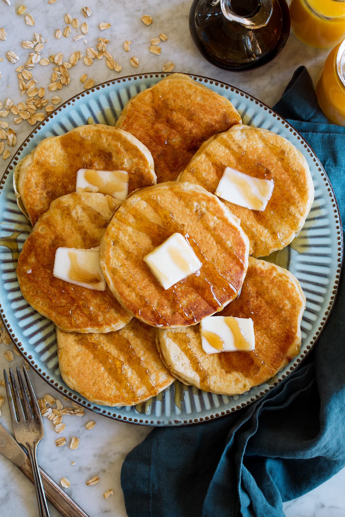 Pancakes shown from overhead. They are spread out on a blue plate, topped with maple syrup drizzle and dabs of butter.