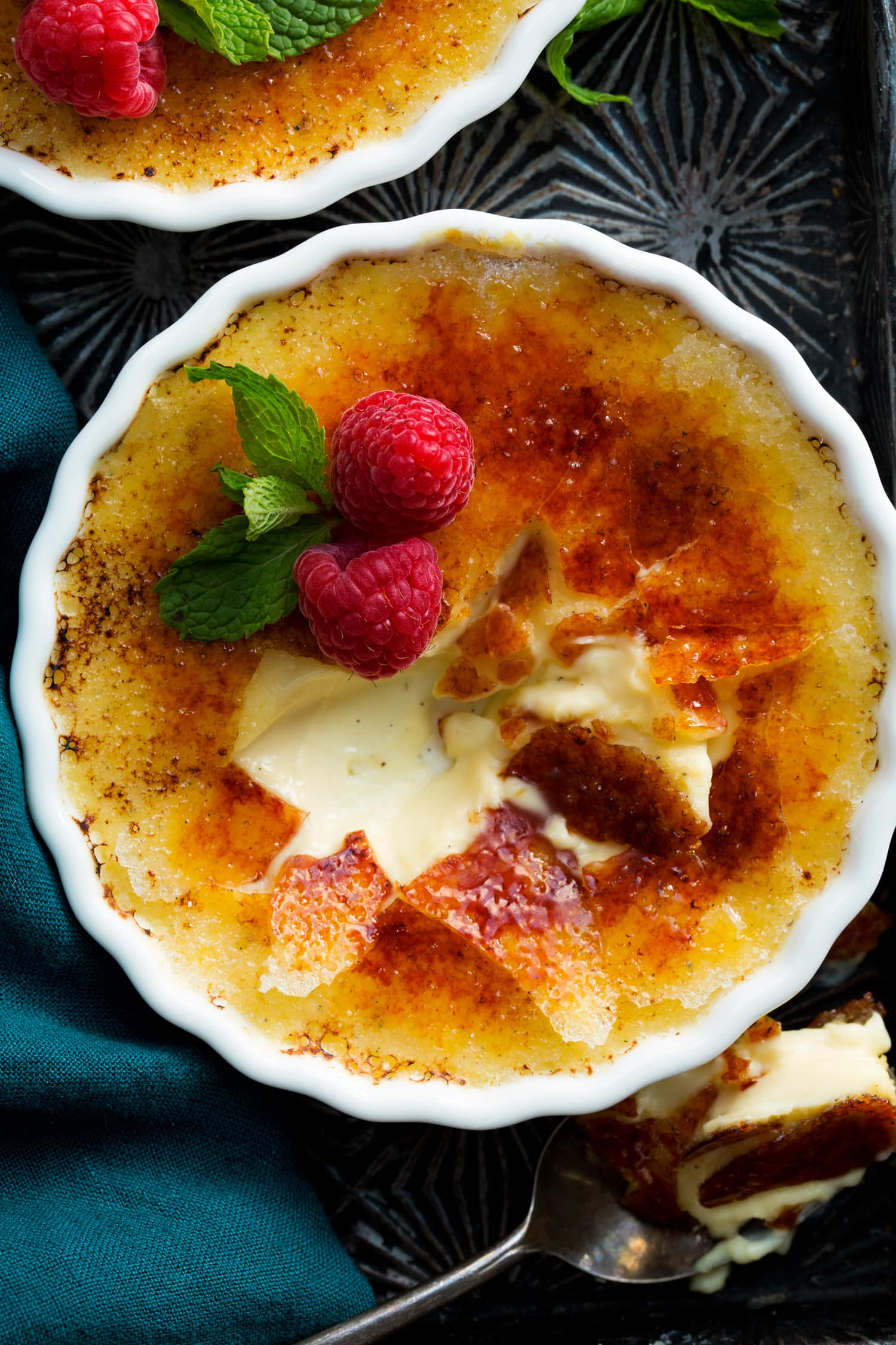 Close up photo of creme brûlée garnished with raspberry and mint.