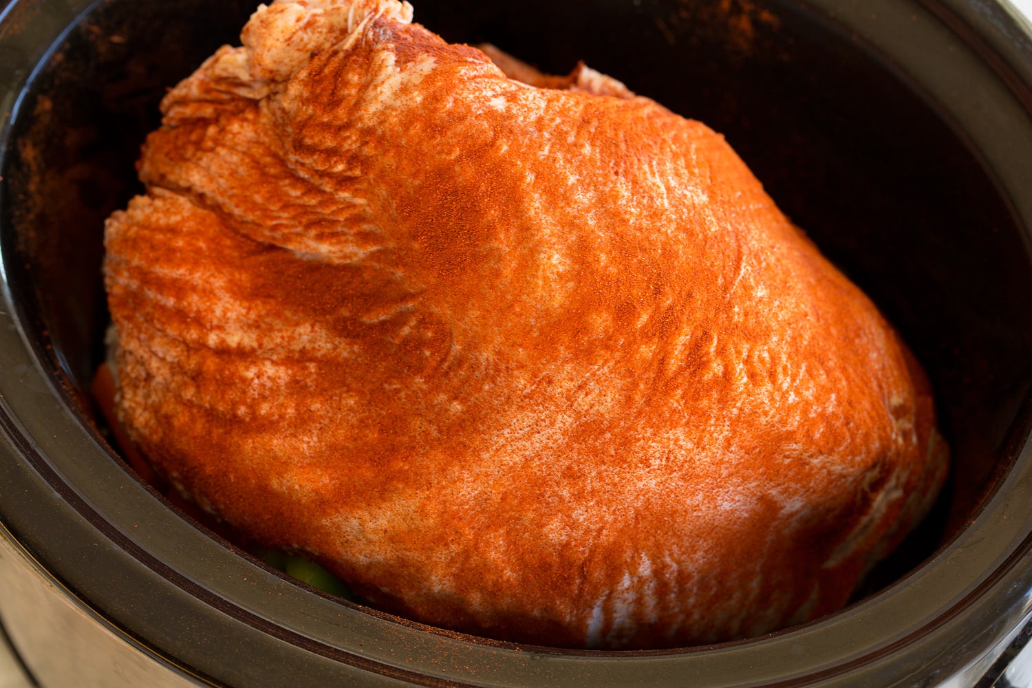 Raw turkey breast being added to slow cooker over veggies.