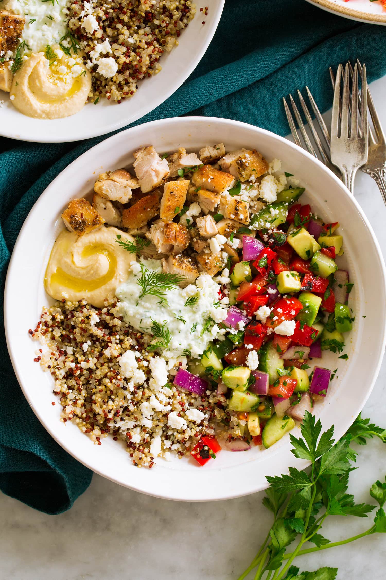 Overhead photo of Greek chicken bowls with diced chicken thighs, greek salad, quinoa, hummus and tzatziki.