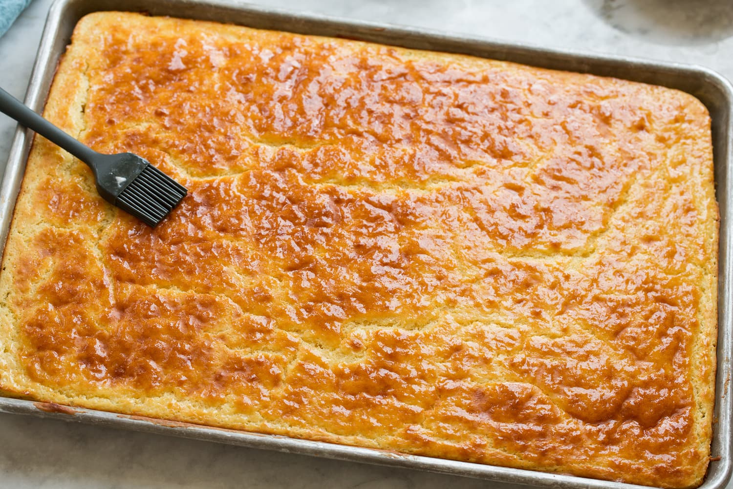 Sheet pan pancake after baking being brushed with melted butter.