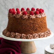 Whole chocolate angel food cake on a white marble and wood cake stand.