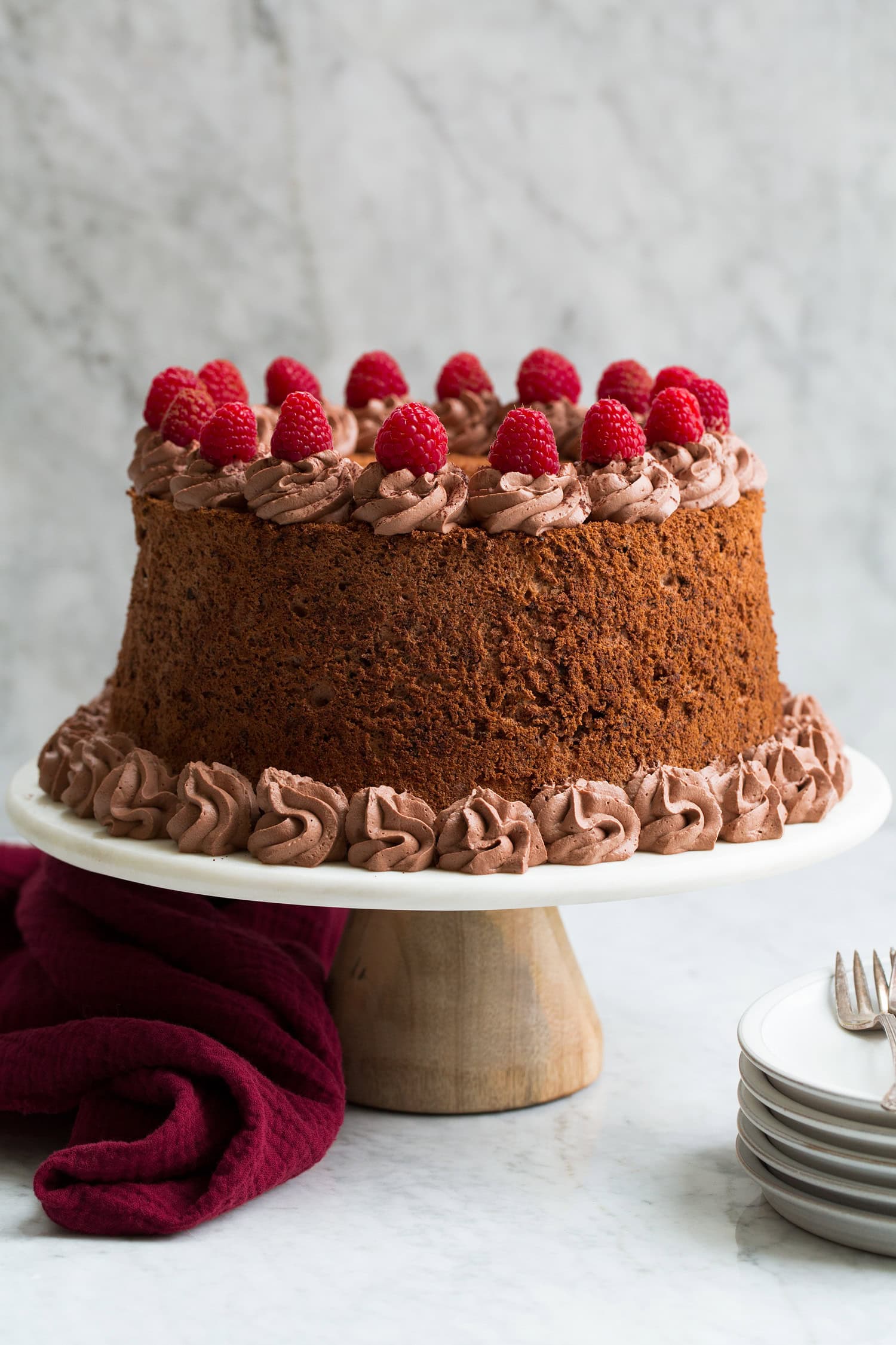 Whole chocolate angel food cake on a white marble and wood cake stand.