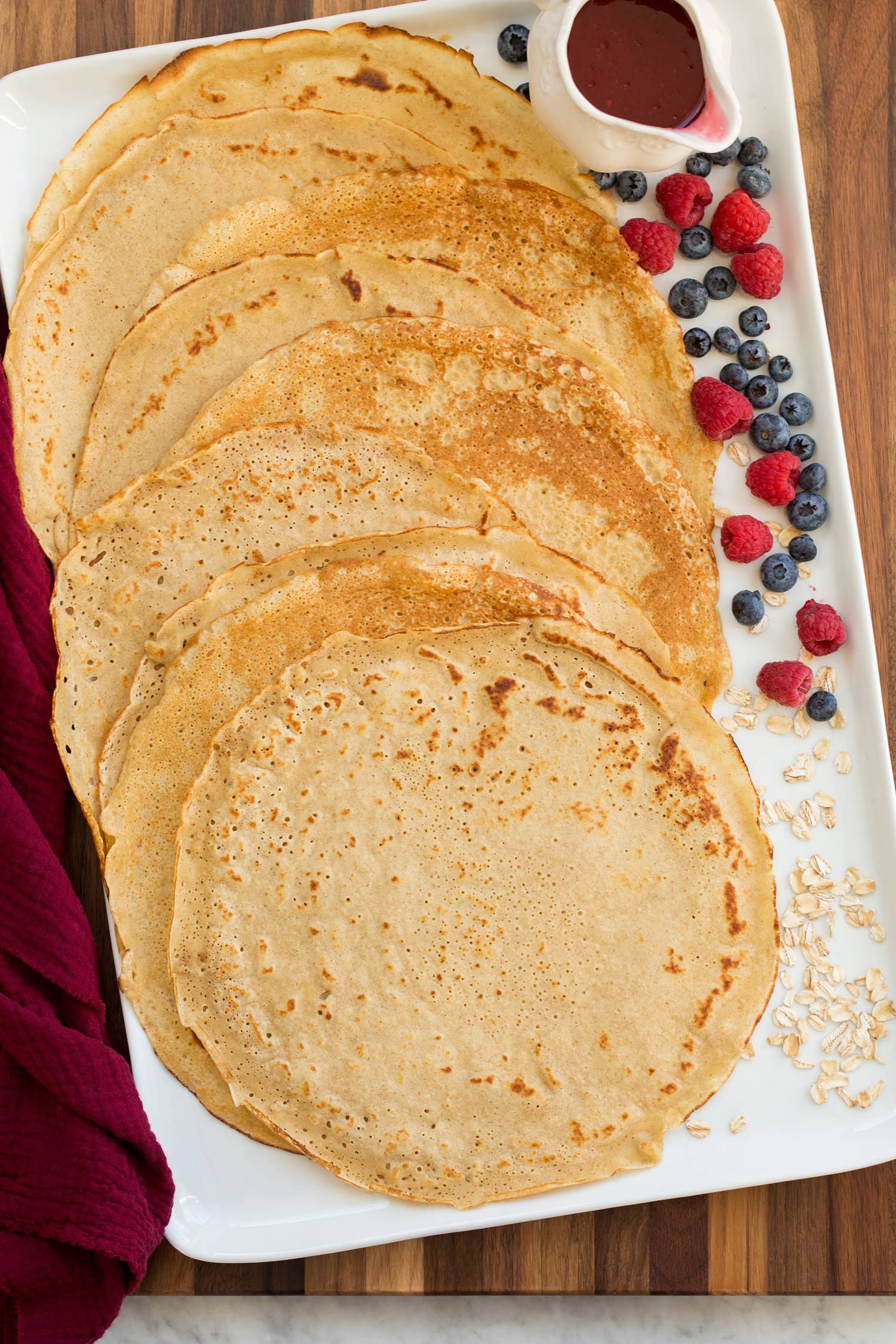 Oat flour crepes shown on a white rectangular platter with fresh fruit to the side.