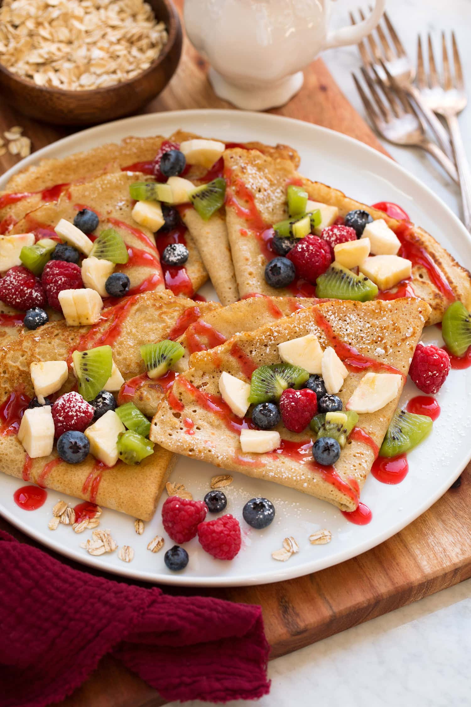 Oatmeal crepes shown folded with fresh fruit and berry syrup drizzled over the top.