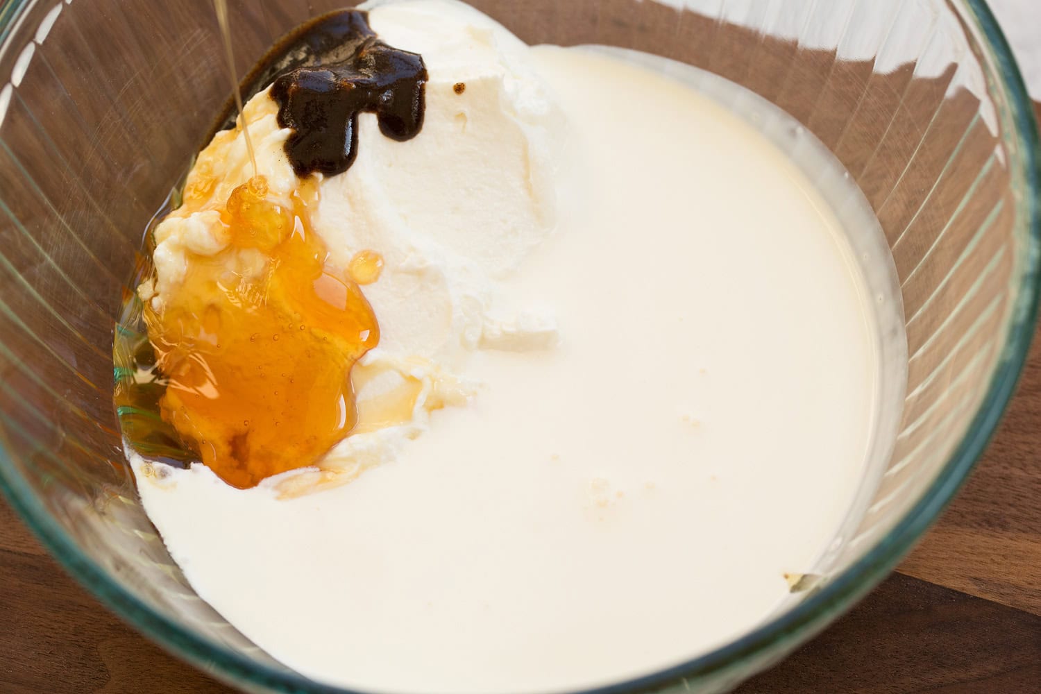 Yogurt, cream, honey and vanilla bean in a mixing bowl.