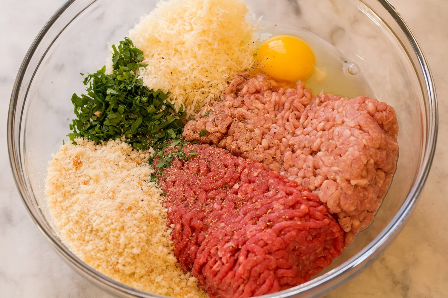 Ground beef, pork, herbs, parmesan, egg and breadcrumbs in a mixing bowl.