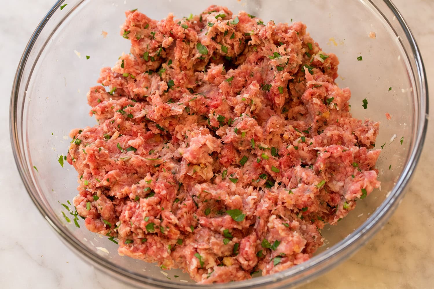Meatball mixture in glass mixing bowl shown after mixing.