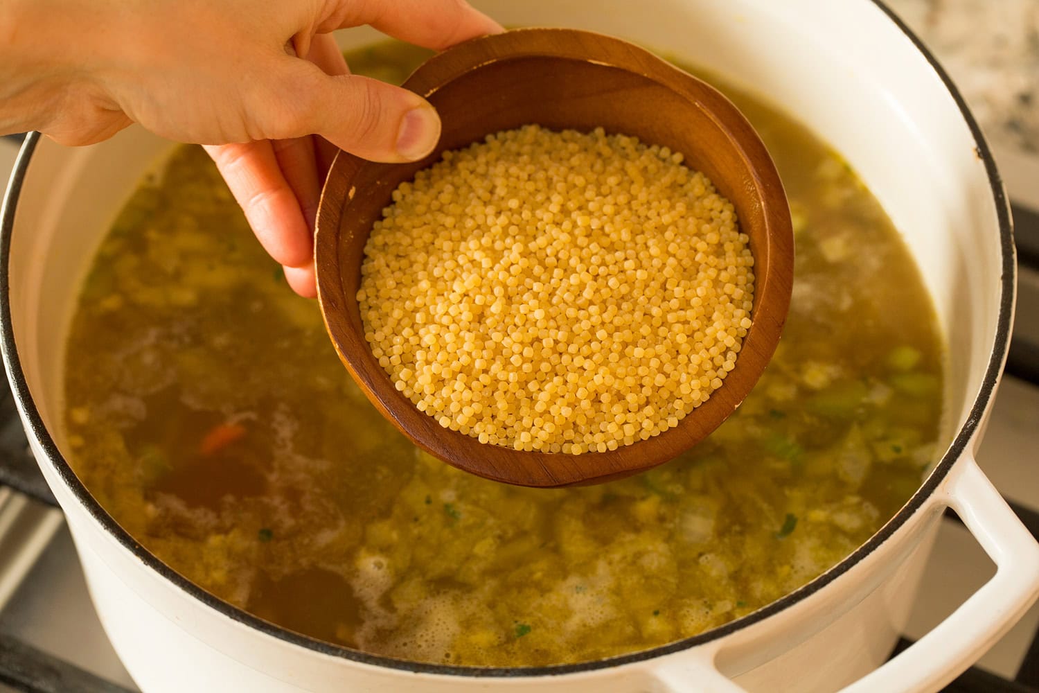 Adding acini di pepe pasta into soup.