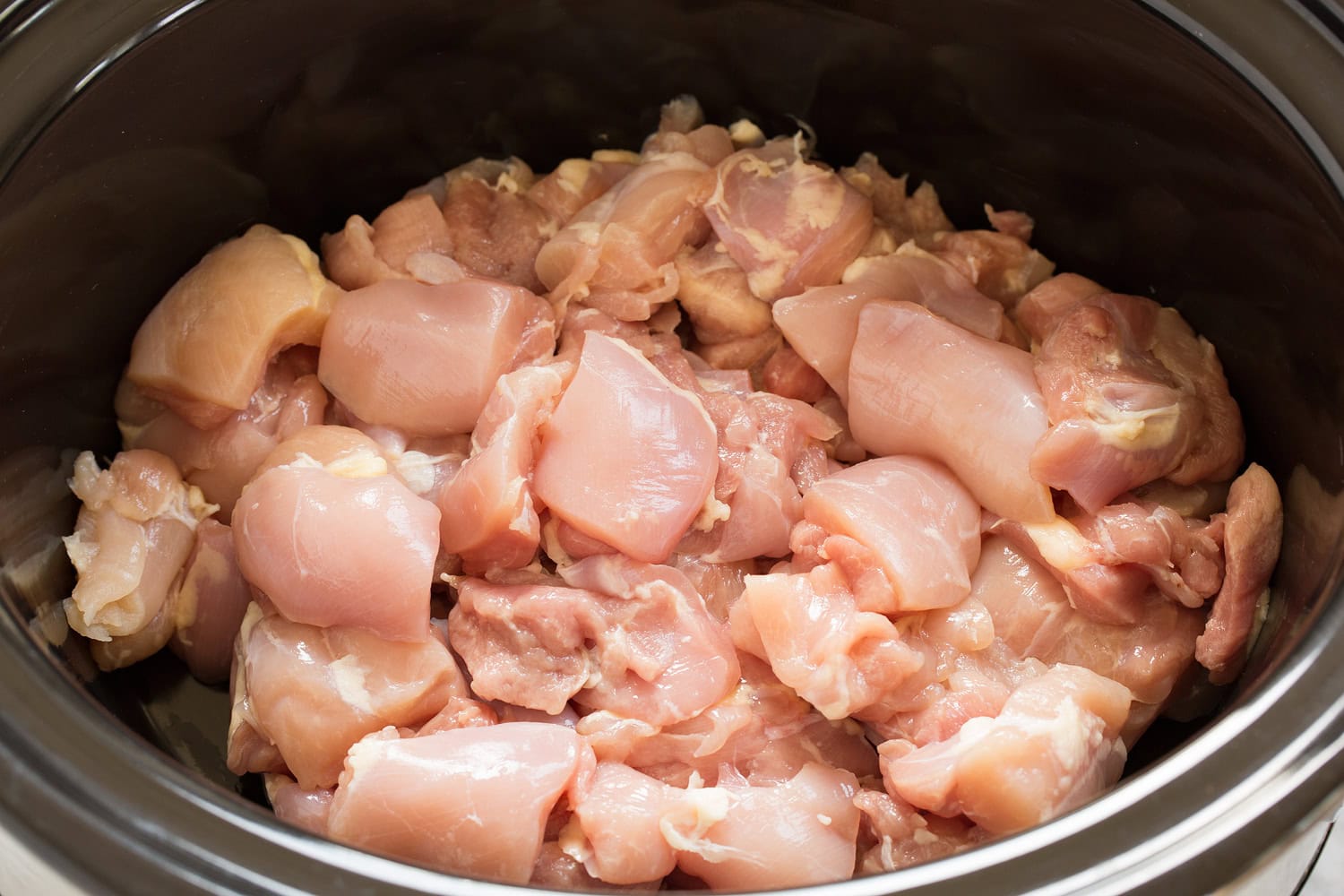 Chicken thighs cut into chunks in a crock pot.