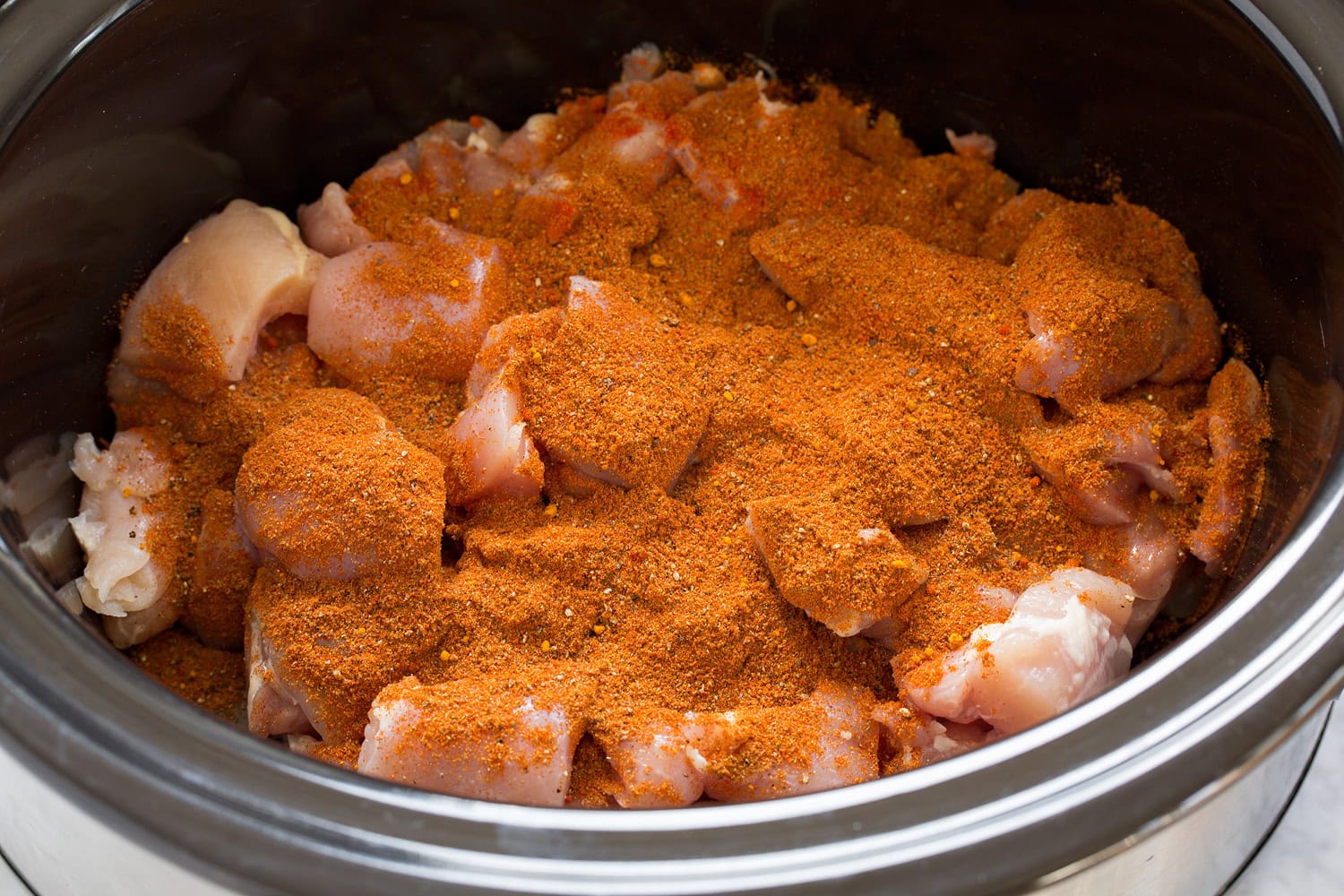 Spices added over chicken thigh chunks in crock pot.