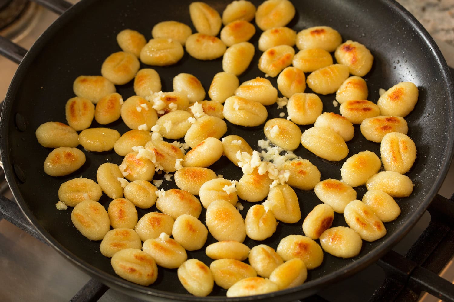 Garlic added to browned sauteed gnocchi in skillet.