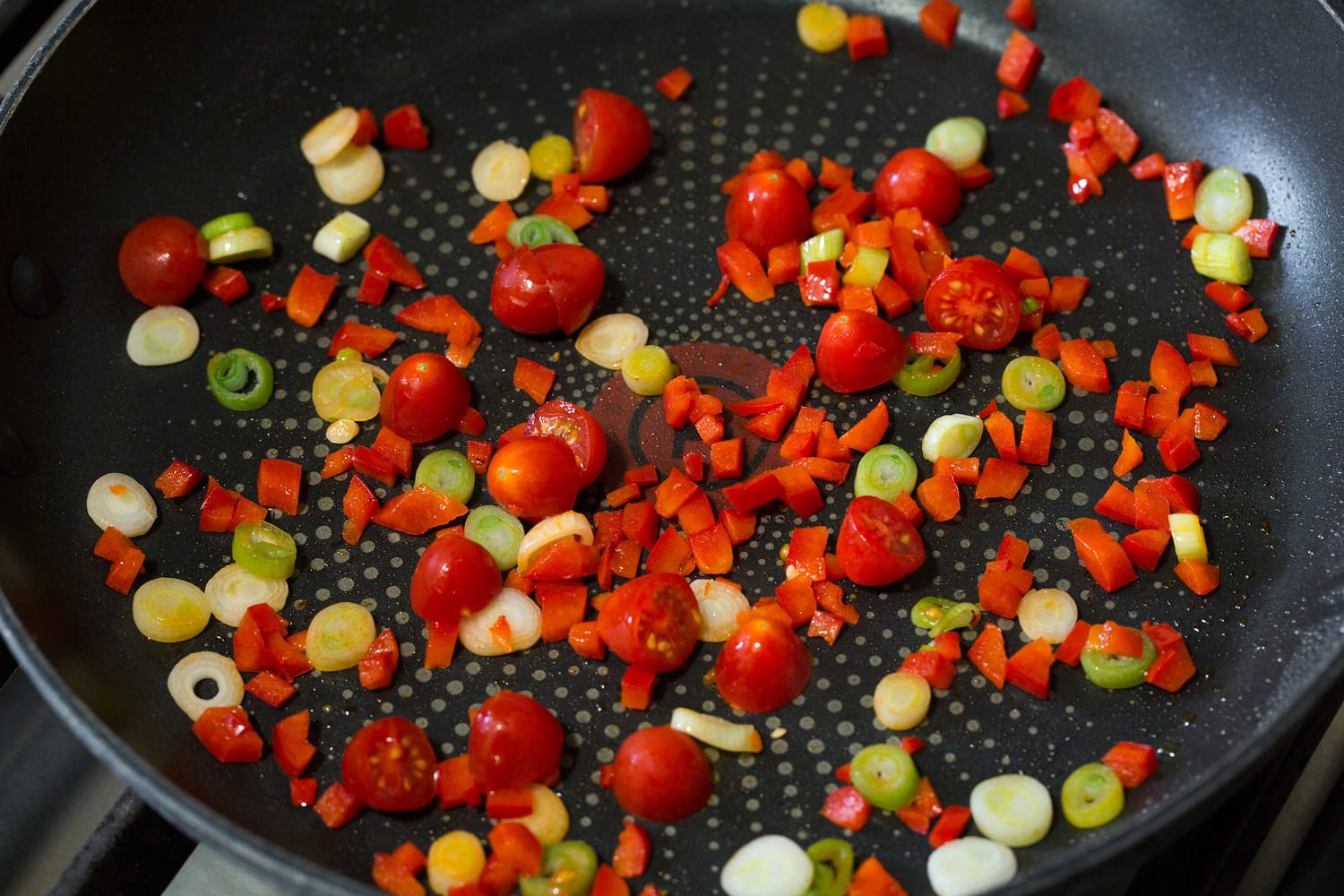 Bell pepper, tomatoes and green onions being sauteed in a skillet.