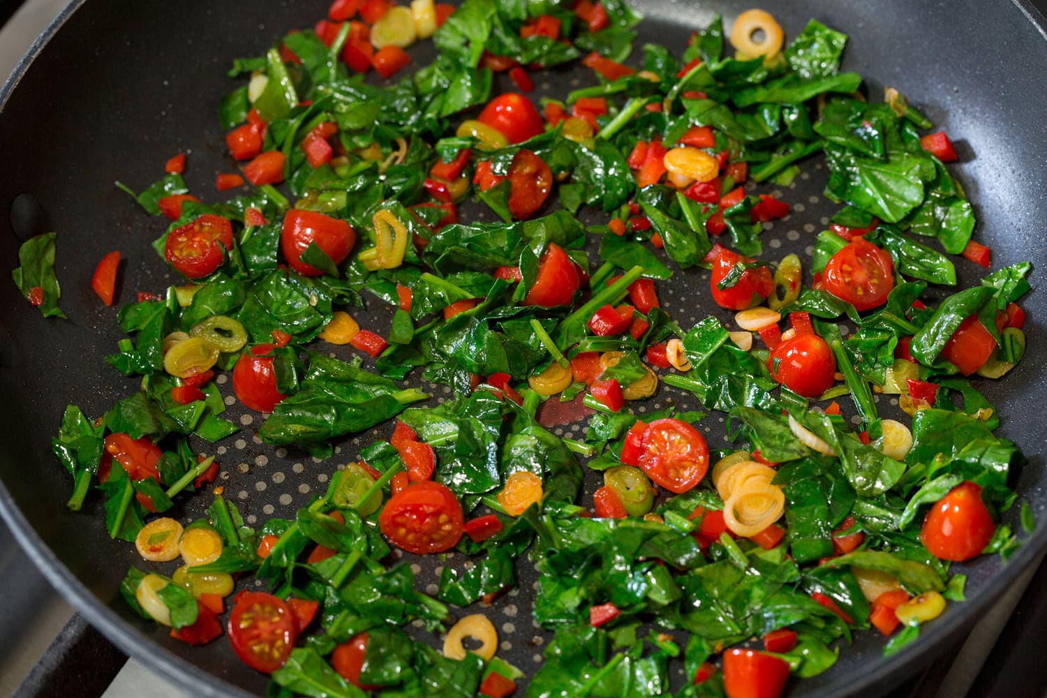 Spinach added to sauteed veggie mixture in skillet.
